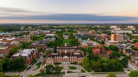 An aerial view of the University of Illinois Urbana-Champaign campus, with leafy walkways, red-brick buildings, and the Main Quad at dusk.